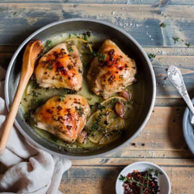 Baked chicken in white wine in the pan. On rustic wooden background, top view