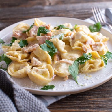 Traditional pasta dish from italy. Tortellini alla panna cooked with ham, parmesan cheese, herbs in a delicious cream sauce. Served isolated on wooden table background