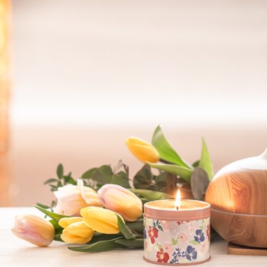 Aromatic oil diffuser lamp on the table on a blurred background with a beautiful spring bouquet of tulips and burning candles .
