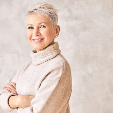 People and aging concept. Portrait of beautiful elegant middle aged woman in warm cozy turtle neck sweater smiling, keeping arms crossed on chest, her posture and look expressing confidence