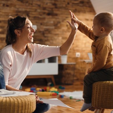 Playful mother and son giving high-five to each other and having fun at home. Focus is on mother.