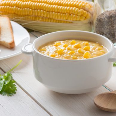 Corn soup in white bowl and toast with corn on white table.