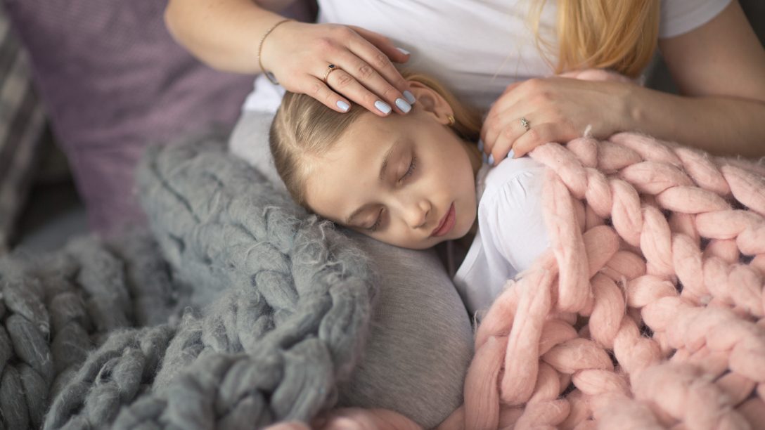 Mother and daughter of a blonde with long hair embrace and acceptance, sleep on the bed in a gray lifestyle in a real interior. Motherhood concept closeup, pastel colors