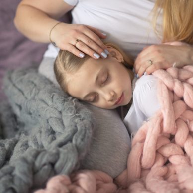 Mother and daughter of a blonde with long hair embrace and acceptance, sleep on the bed in a gray lifestyle in a real interior. Motherhood concept closeup, pastel colors