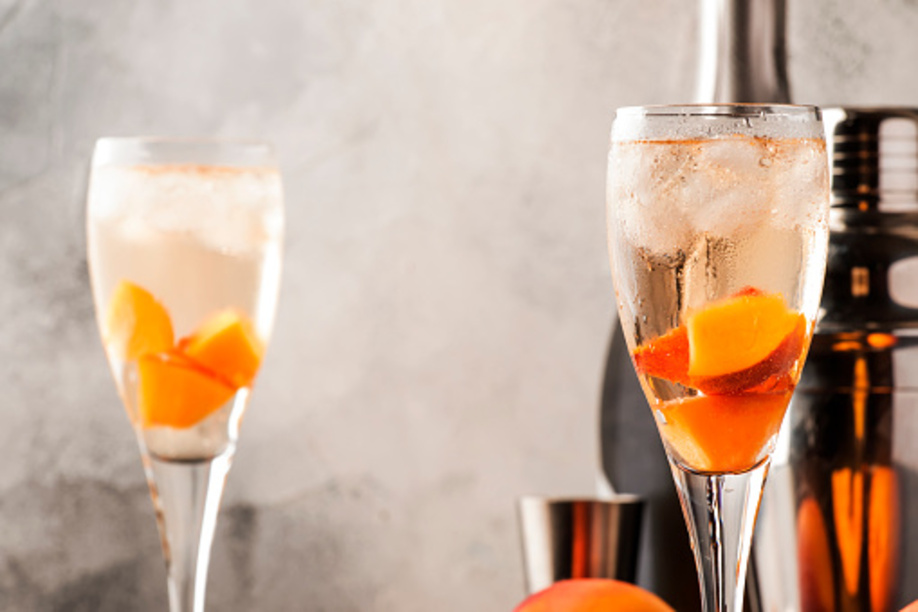 Bellini, alcoholic cocktail with sparkling wine, sugar syrup, lemon juice, peach and ice, gray table background, copy space