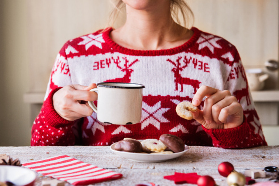 Christmas composition on a vintage wooden background. Unrecognizable woman eating biscuits and drinking coffee.