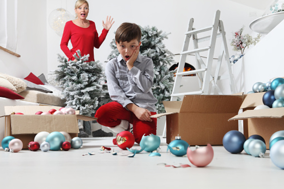 Merry Christmas and Happy Holidays! Mom and son decorate the Christmas tree indoors. accidentally the child breaks the balls, astonished looks at the shards on the floor,while the mother gets angry