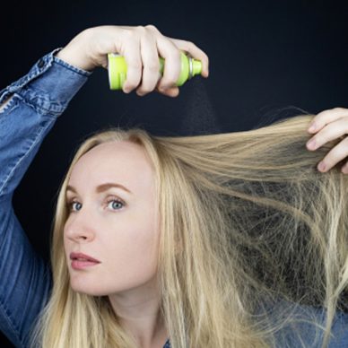 Blonde girl sprays shampoo on her hair. The problem of oily hair while traveling. An emergency remedy for excessive sebum production. Make your head clean without water. Dry shampoo.