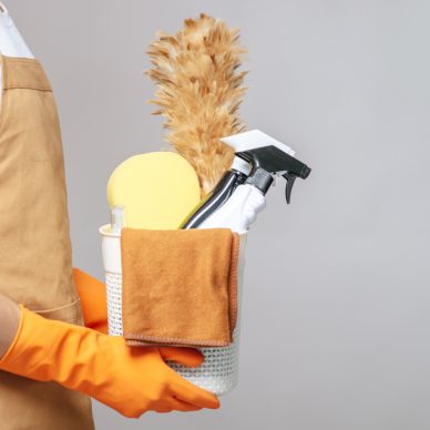 Side view, Close up hand of Young man in apron and rubber gloves holding a basket of cleaning equipment, the feather duster, spray bottle, sponge and cloth for wiping in basket. copy space
