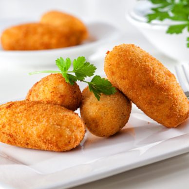 Homemade gourmet croquettes on a white plate with fork.