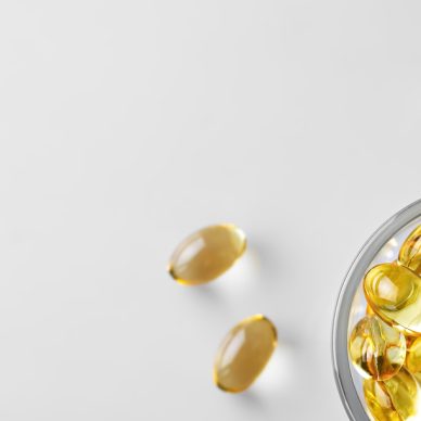 Capsules of fish oil (omega-3) in a glass bowl and on a white stschl nearby. Flat lay with copy space, white background.