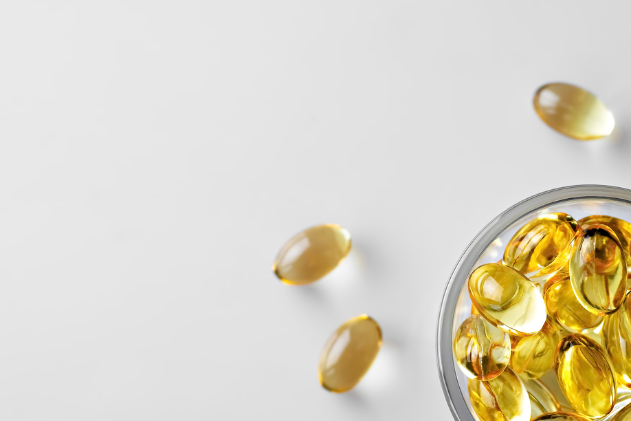 Capsules of fish oil (omega-3) in a glass bowl and on a white stschl nearby. Flat lay with copy space, white background.