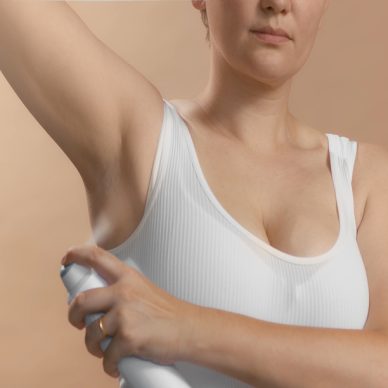 White young european female with lifted hand use antiperspirant to avoid stink and bad smelling. Clean seamless white bra. Studio high quality photo image on beige background.