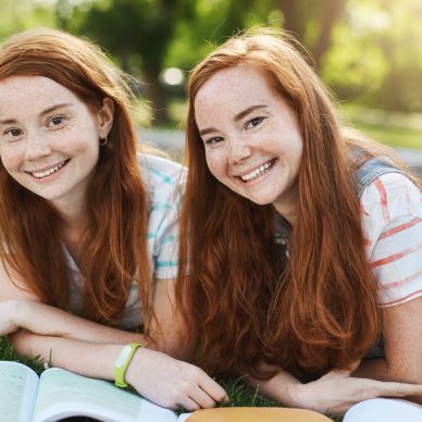 Ginger twin girls spending their summer school break to get ready to university exams. Future doctor and lawyer having fun smiling on a sunny day in park.