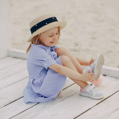 a cute little girl in a blue dress and a straw hat playing on the beach