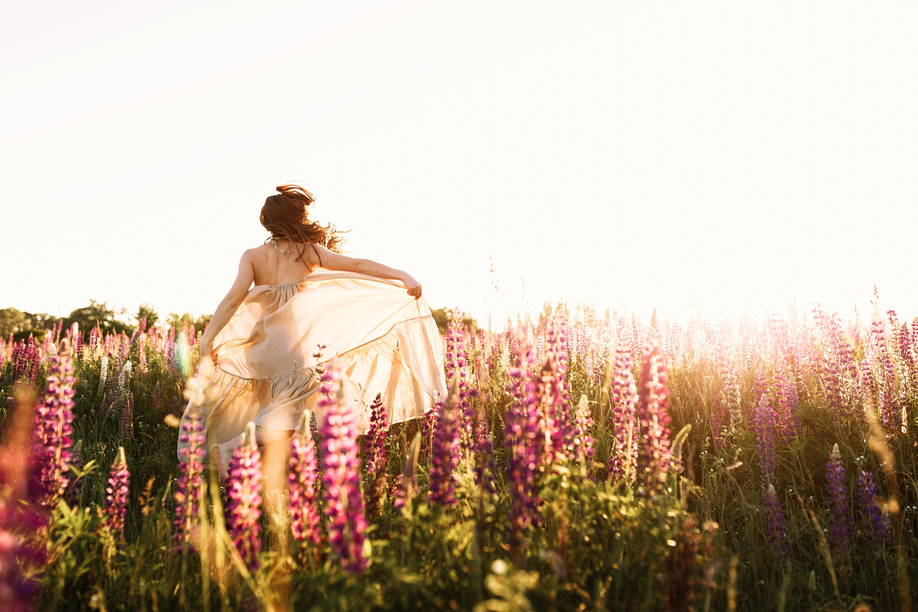 A beautiful bride in wedding dress is dancing alone in a field of wheat. View from the back