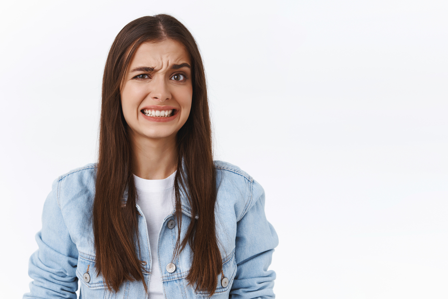 Girl cringe as seeing something embarrassing and bothering. Woman make uncomfortable smile and squinting feeling worried and displeased, see bothering bad situation, standing white background.