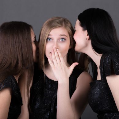 Three young girlfriends gossiping, teenage girl looks shocked as two her friends are murmuring rumors in her ears