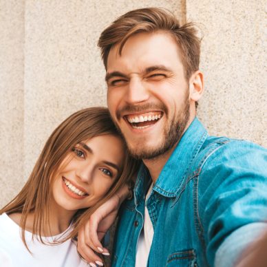 Smiling beautiful girl and her handsome boyfriend in casual summer clothes. Happy family taking selfie self portrait of themselves on smartphone camera. Having fun on the street background