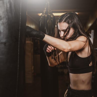 Skinny focused woman has a boxing training with punching bag at dark gym.