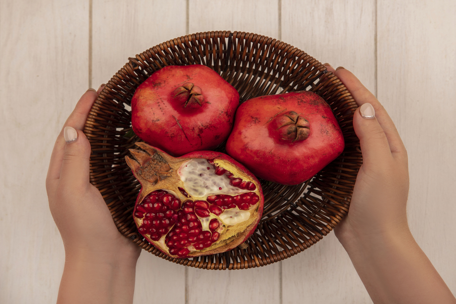 top view woman holding pomegranates in a basket on a white background