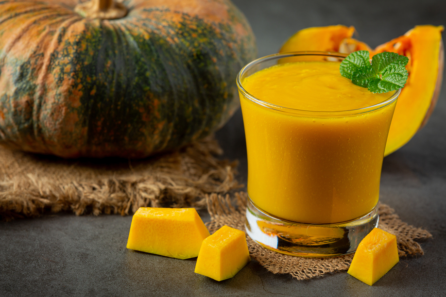 a glass of pumpkin juice and chopped raw pumpkins place on dark floor