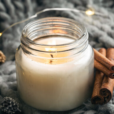 An aromatic candle and cinnamon on grey knitted background. Aromatherapy, atmosphere of cosiness and relax.