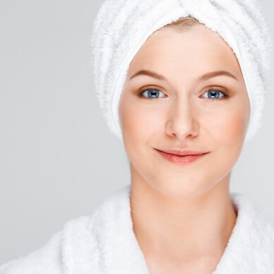 Portrait of blonde young pretty girl in bathrobe with towel on head, smiling, looking at camera, over white background.