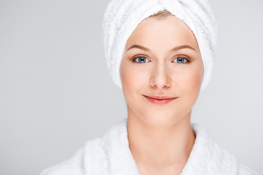 Portrait of blonde young pretty girl in bathrobe with towel on head, smiling, looking at camera, over white background.