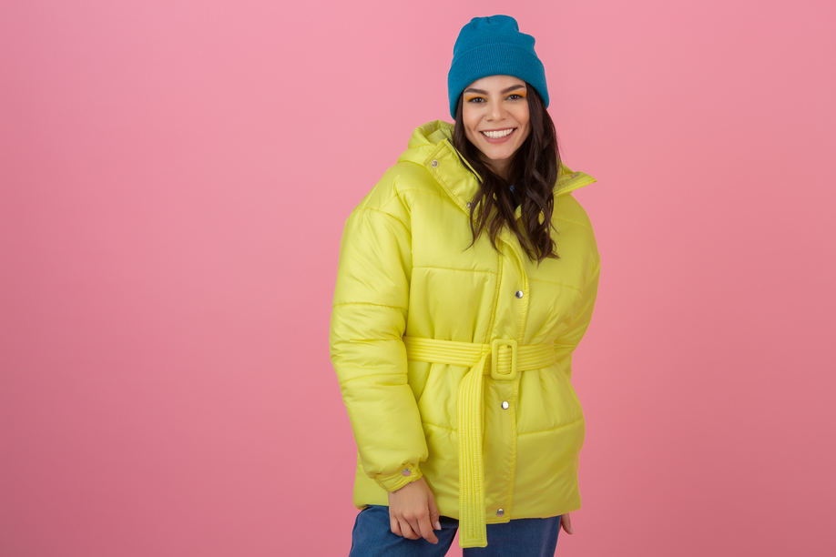 attractive active woman posing on pink background in colorful winter down jacket of bright ryellow color, smiling fun, warm coat fashion trend