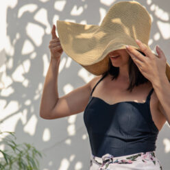 Young woman hides her face from the rays of the sun under a large straw hat.