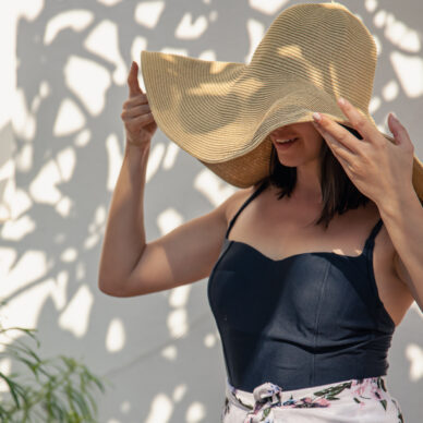 A girl in a large straw hat in front of a wall covered with a curly old tree.