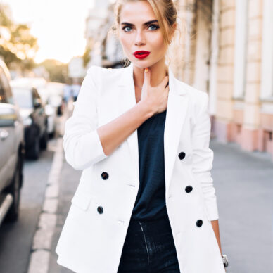 Portrait fashion model walking in city. She wears white jacket, looking to camera