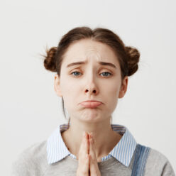 Portrait of girl 20s with upset look begging for mercy being disappointed with praying gestures. Capricious female with brown hair in double buns pouting having hopeful expression. Close up