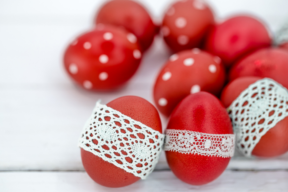 Red Easter eggs on white background tied lace tape , close-up , lying on a white wooden background still life