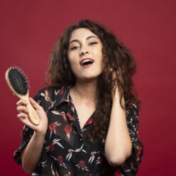 Curly woman holding comb on red background