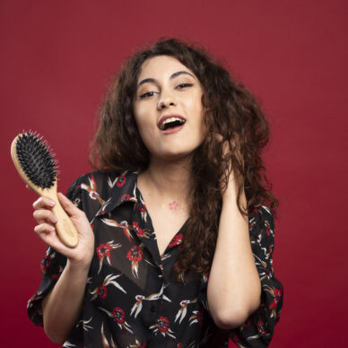 Curly woman holding comb on red background. High quality photo