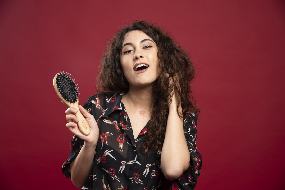 Curly woman holding comb on red background. High quality photo