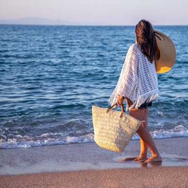 A girl with a hat in her hands and a wicker bag walks on the seashore. Summer vacation concept.
