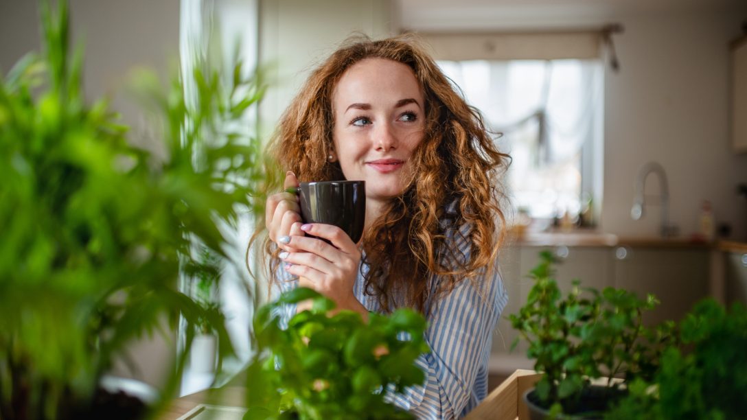 Front view of young woman relaxing indoors at home with cup of coffee or tea.