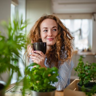 Front view of young woman relaxing indoors at home with cup of coffee or tea.