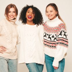 Three young beautiful smiling hipster girls in trendy winter sweaters. Sexy carefree women in studio. Positive models having fun and hugging