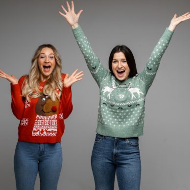 female caucasian friends in warm sweaters rejoice together, picture isolated on grey background