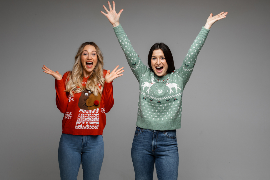 female caucasian friends in warm sweaters rejoice together, picture isolated on grey background