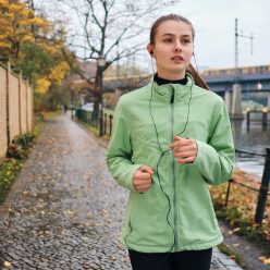 Beautiful sporty girl in earphones running with music around par