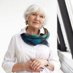 Isolated view of successful positive beautiful businesswoman with gray hair standing in confident posture against white office wall background with copyspace for your text or advertising content