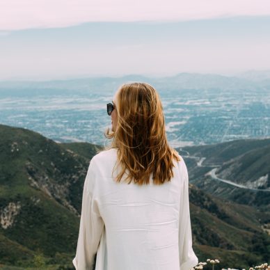 A beautiful blonde-haired female with sunglasses and a white shirt standing on top of a hill in nature