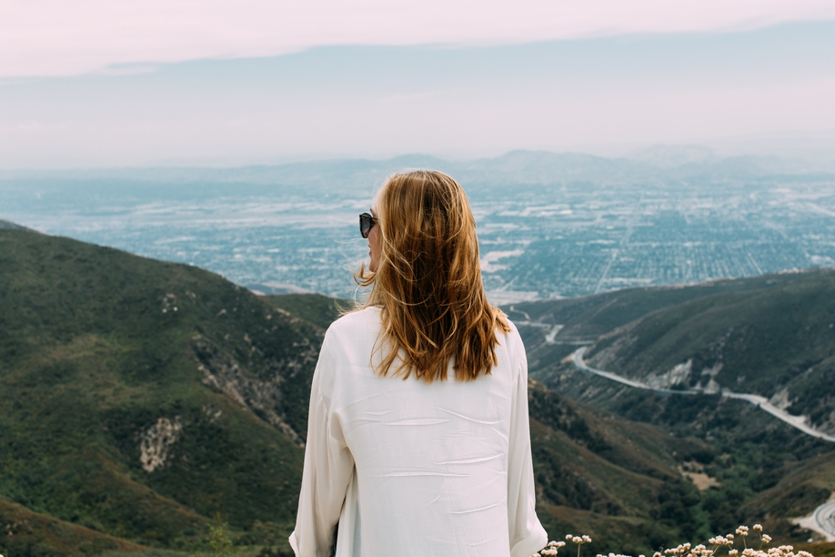 A beautiful blonde-haired female with sunglasses and a white shirt standing on top of a hill in nature