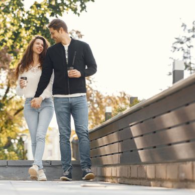 Cute couple in a city. Man in a black jacket. People walks. Girl drinks a coffee.