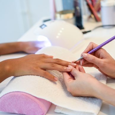 Close-up of beautician painting a woman's nails with a brush in a nail salon. Costumer receiving a manicure.